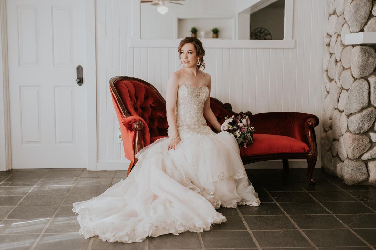 bridal hair and makeup — bride seated on vintage red settee